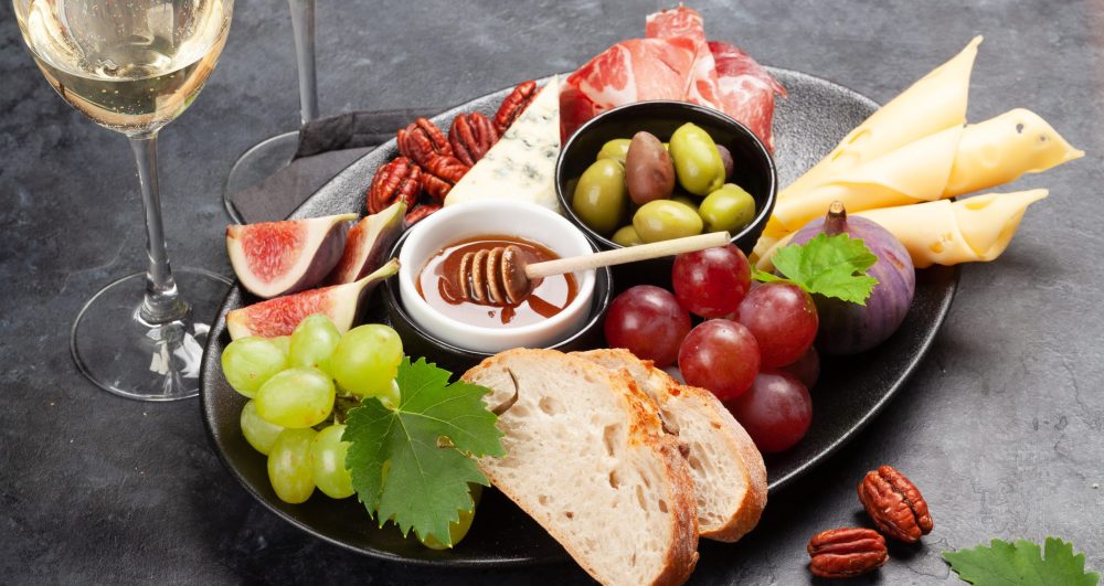 Antipasto plate with prosciutto, cheese, figs and grapes. Appetizer board and white wine