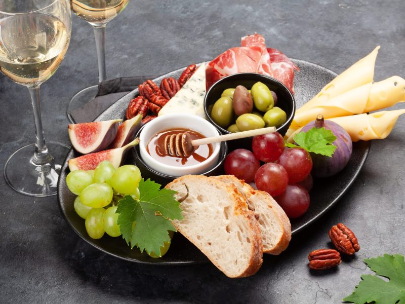 Antipasto plate with prosciutto, cheese, figs and grapes. Appetizer board and white wine